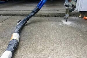 A machine is injecting material into a crack in a concrete driveway for repair. The hose is connected to the injection device placed near the crack.